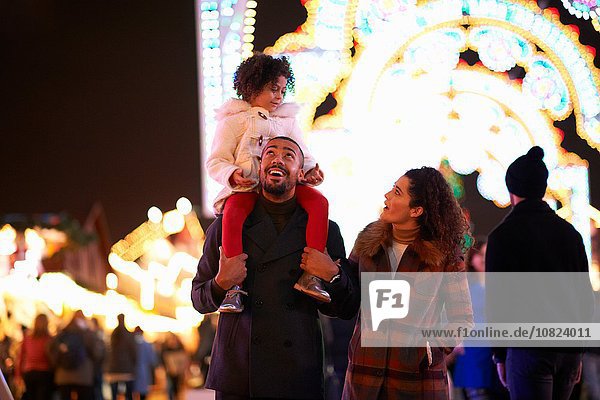 Young family at funfair  father carrying daughter on shoulders