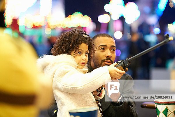 Father helping daughter with rifle at shooting gallery at funfair