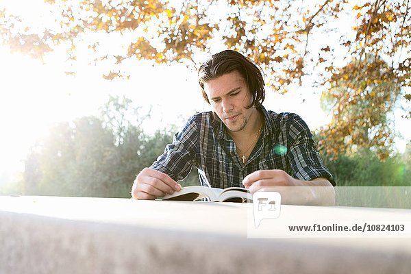 Young man outdoors sitting at table looking down reading book