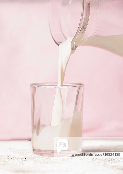 Gießen von Milch in Glas  rosa Hintergrund