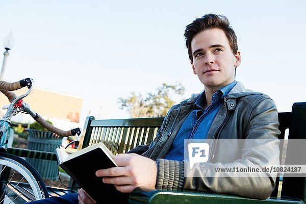 Young man reading book on park bench