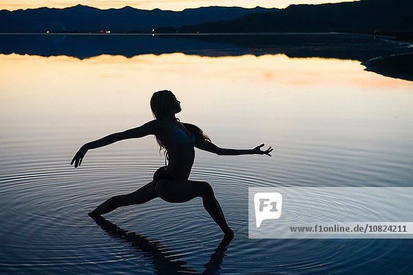 Silhouetted female dancer poised with open arms in lake at sunset  Bonneville Salt Flats  Utah  USA