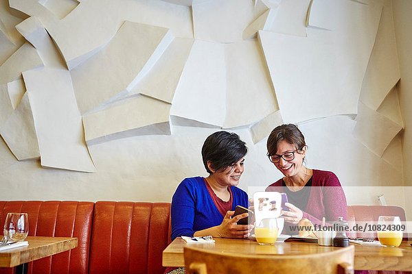 Zwei erwachsene Freundinnen beim Lesen von Smartphone-Texten im Restaurant