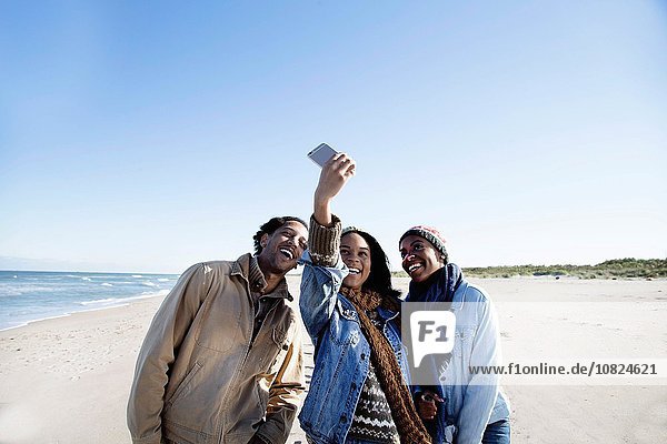 Three friends on beach  taking self portrait  using smartphone