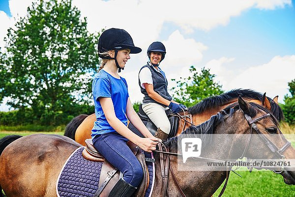 Seitenansicht der reifen Frau und des Mädchens zu Pferd mit lächelndem Reiterhut