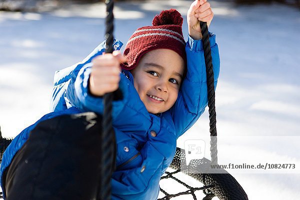 Preschool boy wearing knit hat on hammock swing  looking at camera smiling