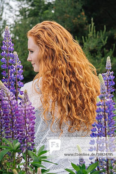 Rückansicht Porträt einer jungen Frau mit langen roten Haaren unter lila Wildblumen