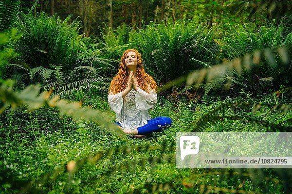 Junge Frau praktiziert Yoga in Lotusstellung im Wald
