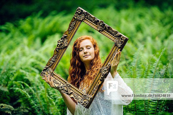 Junge Frau mit goldenem Bilderrahmen zwischen Waldfarnen