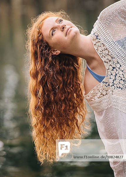Porträt einer ruhigen jungen Frau mit langen roten Haaren  die aus dem Fluss blickt.