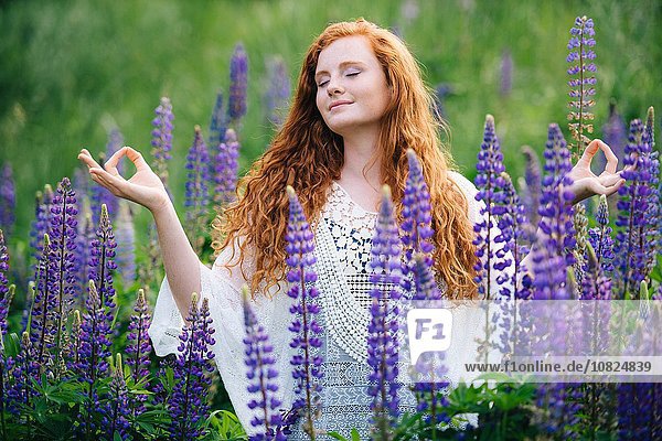 Gelassene junge Frau beim Meditieren unter lila Wildblumen