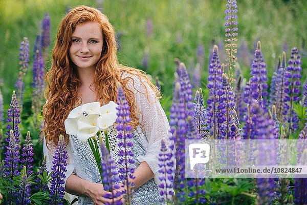 Porträt einer jungen Frau inmitten violetter Wildblumen mit Lilienstrauß