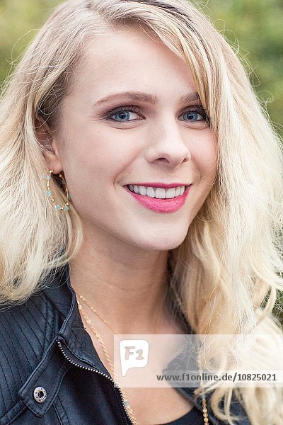 Nahaufnahme Porträt einer jungen blonden Frau in Lederjacke mit lächelndem Blick auf die Kamera