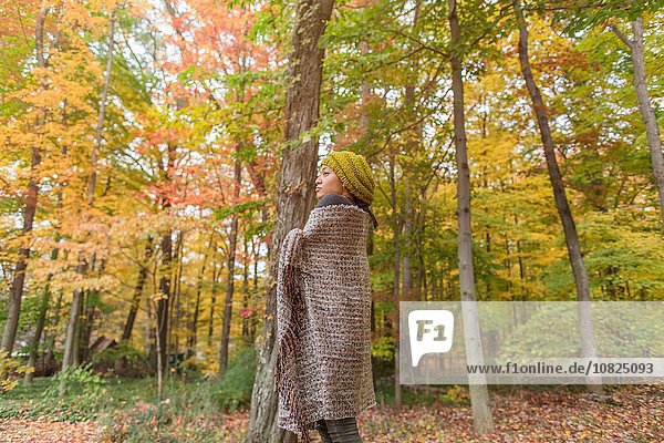 Mid adult woman wrapped in shawl standing in autumn forest