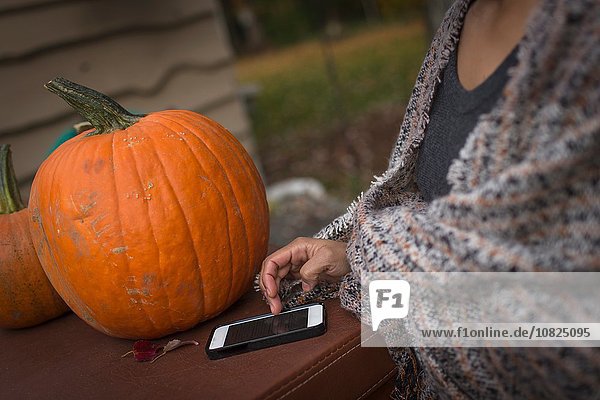 Ausschnitt einer mittelgroßen Frau mit Smartphone-Touchscreen im Garten