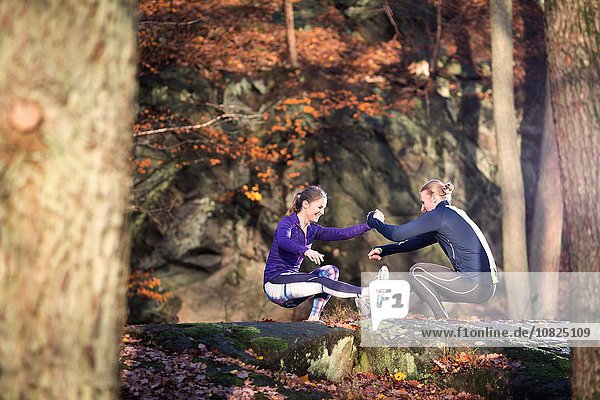 Seitenansicht des Paares auf Felsen im Wald von Angesicht zu Angesicht  Händchen haltend  hockend auf einem Bein balancierend