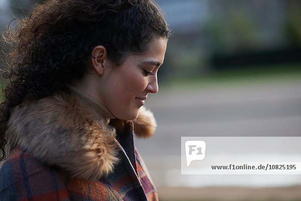 Side view of curly haired woman wearing tartan fur trim coat looking down smiling
