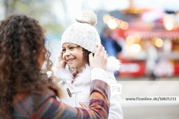 Mother putting knit hat on smiling daughter