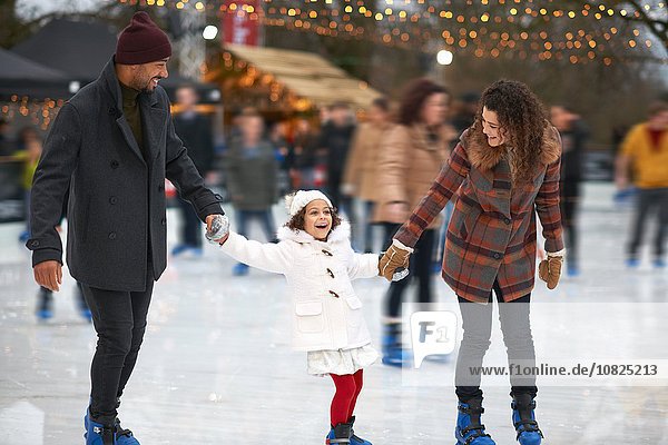 Girl holding parents hands ice skating  smiling