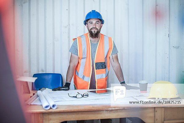 Portrait of young male construction worker standing at desk in portable cabin