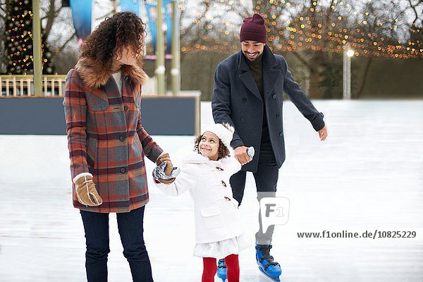 Girl ice skating  holding hands with parents looking up smiling