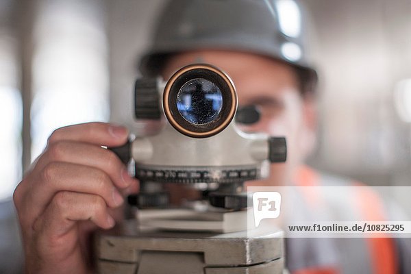 Close up of young male surveyor looking through theodolite on construction site