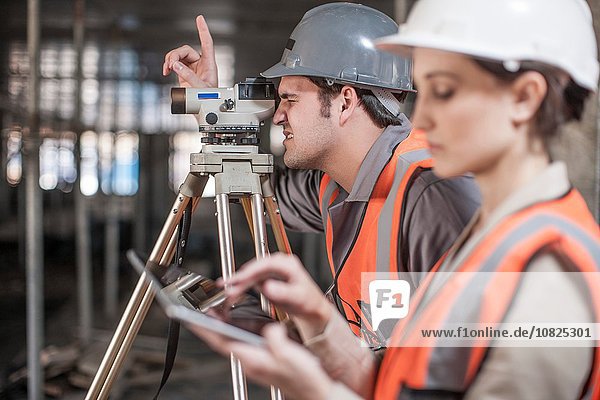 Female and male surveyor using digital tablet and theodolite on construction site