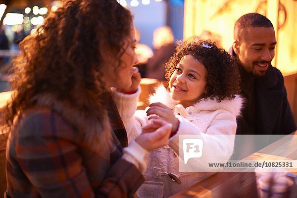 Girl at amusement park sitting at table with parents smiling