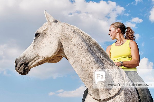 Low angle view of woman riding grey horse bareback against blue sky