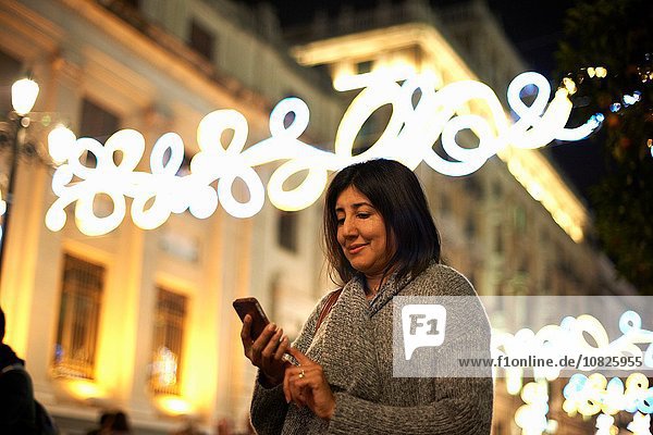 Frau mit Smartphone  dekorative Beleuchtung im Hintergrund  Sevilla  Spanien