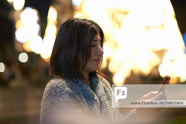 Frau mit Smartphone  dekorative Beleuchtung im Hintergrund