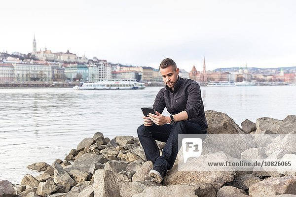 Young man sitting on rocks using digital tablet  Budapest  Hungary