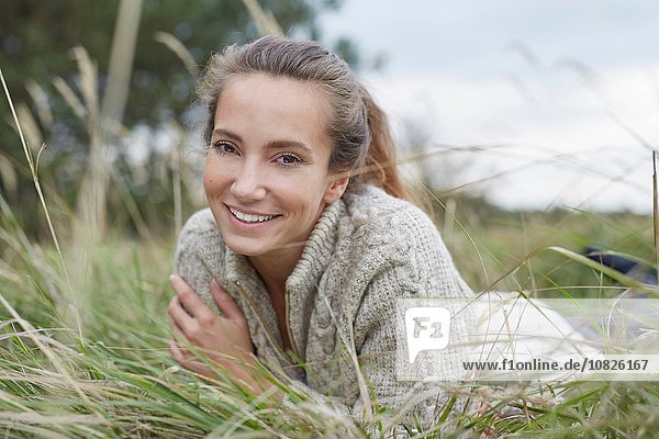 Junge Frau vorne auf Gras liegend mit lächelndem Blick auf die Kamera