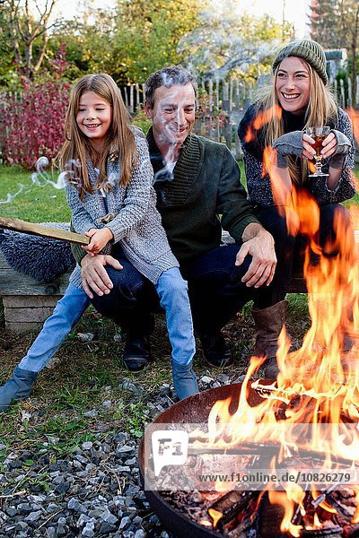 Mädchen mit Mutter und Vater sitzend im Garten mit Feuerstelle