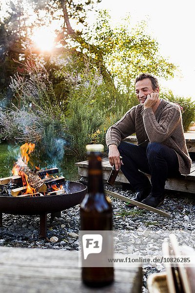 Reifer Mann am Feuer mit Bier sitzend  entspannend