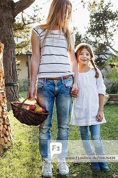 Mother and daughter holding hands  mother holding basket of apples