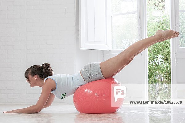 Junge Frau trainiert zu Hause auf rosa Übungsball