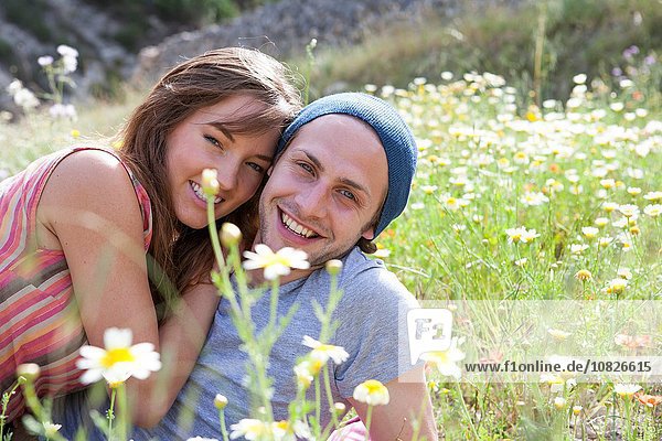 Porträt eines glücklichen jungen Paares  das im Feld der Wildblumen liegt.