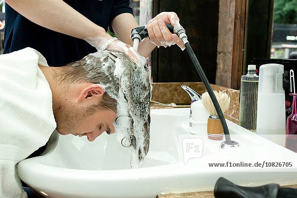 Seitenansicht des jungen Mannes beim Haarewaschen im Friseursalon