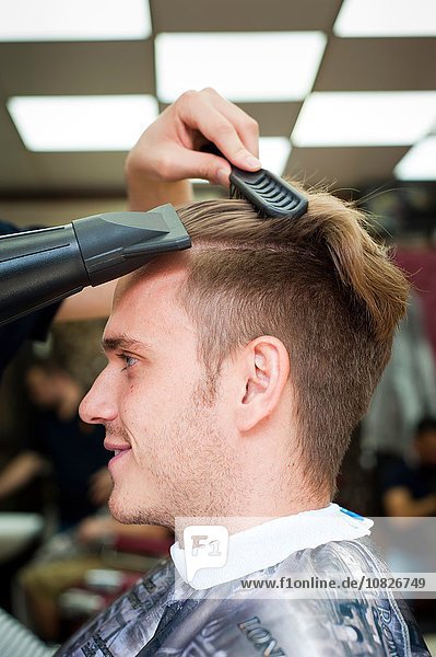 Side view of young man in barbershop having hair blow dried