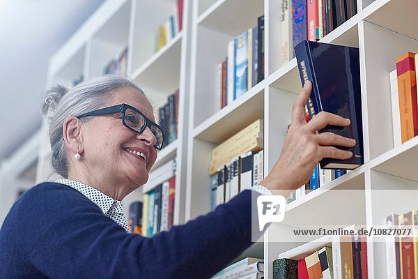Grauhaarige reife Frau  die ein Buch aus dem Bücherregal auswählt