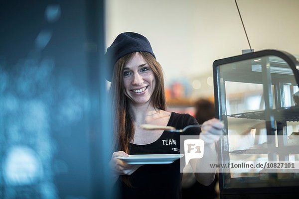 Porträt der jungen Kellnerin mit Teller und Kuchenscheibe im Café