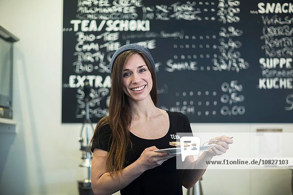 Porträt der jungen Kellnerin mit Teller und Kuchenscheibe im Café