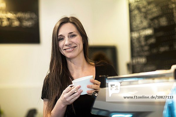 Porträt einer jungen Kellnerin mit Kaffeetasse im Cafe