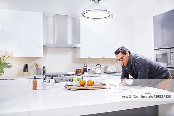 Young man reading newspaper at kitchen counter
