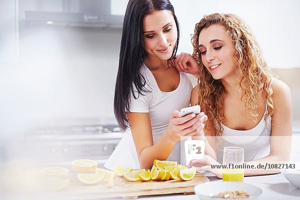 Zwei junge Frauen lesen Smartphone-Text an der Küchenzeile