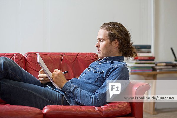 Mann beim Schreiben von Notizen auf der Couch