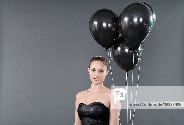 Junge Frau mit schwarzen Luftballons,  grauer Hintergrund