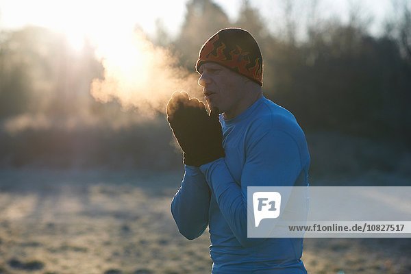 Läufer mit Strickmütze und Handschuhen  Hände aneinander reiben  kalte Luft atmen