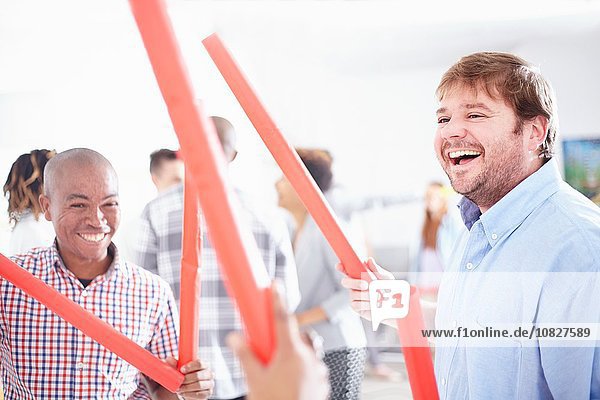 Kollegen in der Teambuilding-Aufgabe  die rote Röhren lächelnd halten